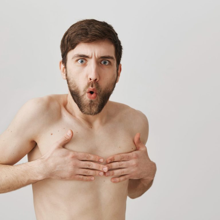 Turn around don't you see I am naked. Funny european man with beard standing naked over gray background and covering nipples with hands, expressing embarrassment and offence, being caught undressed.