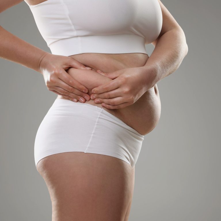 Woman touching belly fat on grey background, closeup. Overweight problem